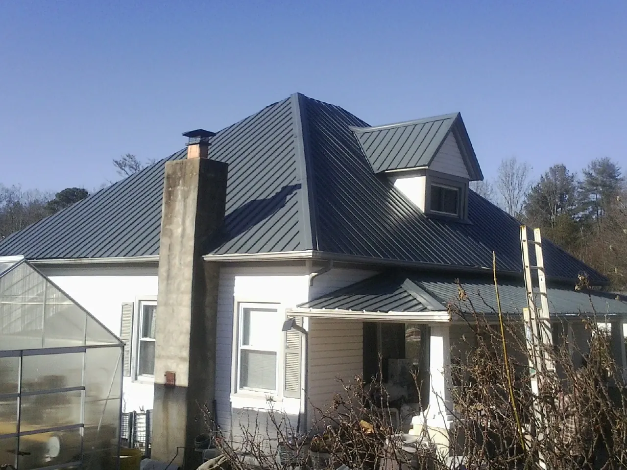 Dark blue standing seam metal roof on a white farmhouse with dormer — Slate & Tile Roof Repair by Roofing Brothers in Runnells