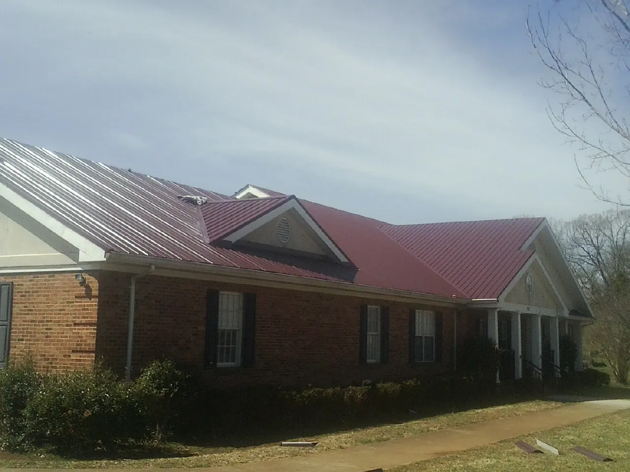Red metal roof with gabled entries on a long brick building, from a Hail Damage Roof Repair job in Runnells