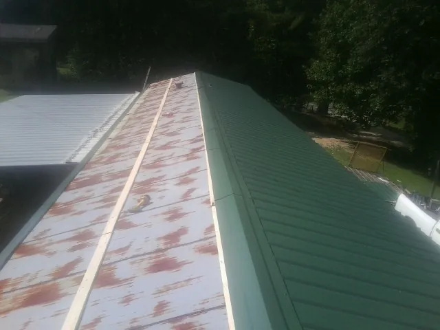 Old rusted panels beside newly installed green metal roofing — Wind Damage Roof Repair by Roofing Brothers in Runnells