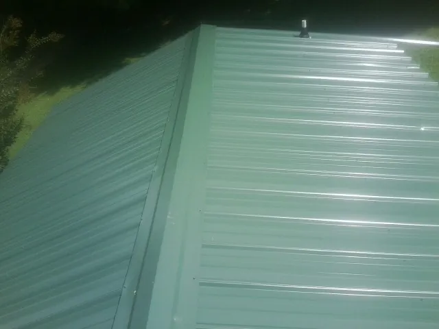 New green metal panels meeting at the ridge of a roof — Flat Roof Repair work by our crew in Runnells