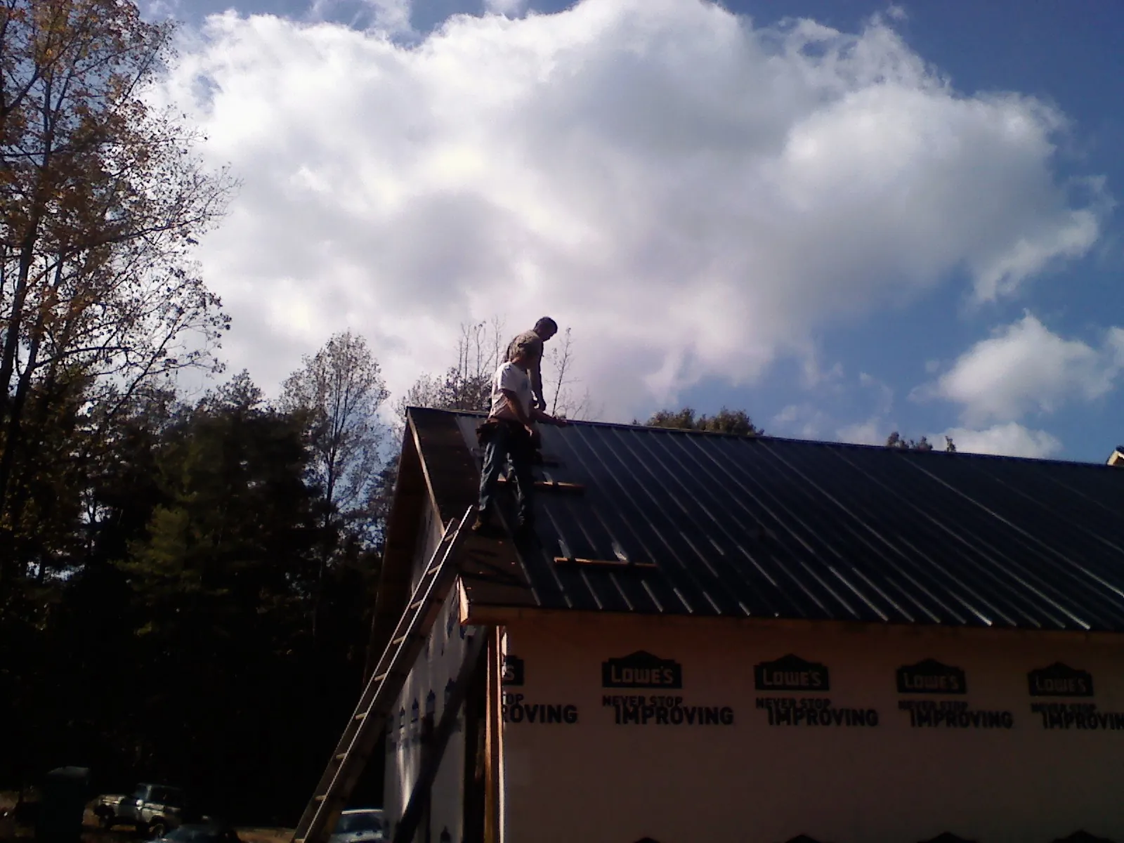 Roofer fastening dark metal panels high against a cloudy sky, from a Roof Inspection job in Runnells