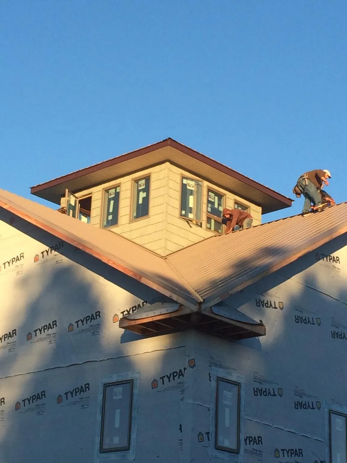 Roofers working around a rooftop cupola on a new metal roof at sunset — Roof Waterproofing in Runnells by Roofing Brothers